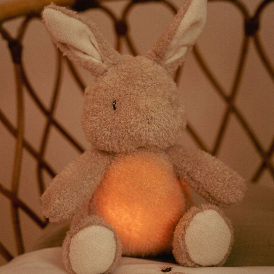 Kanin bamse og natlys i et. Sød krammekanin med beroligende hjerteslag og andre velkendte lyde, set i seng på børneværelse.