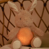 Kanin bamse og natlys i et. Sød krammekanin med beroligende hjerteslag og andre velkendte lyde, set i seng på børneværelse.