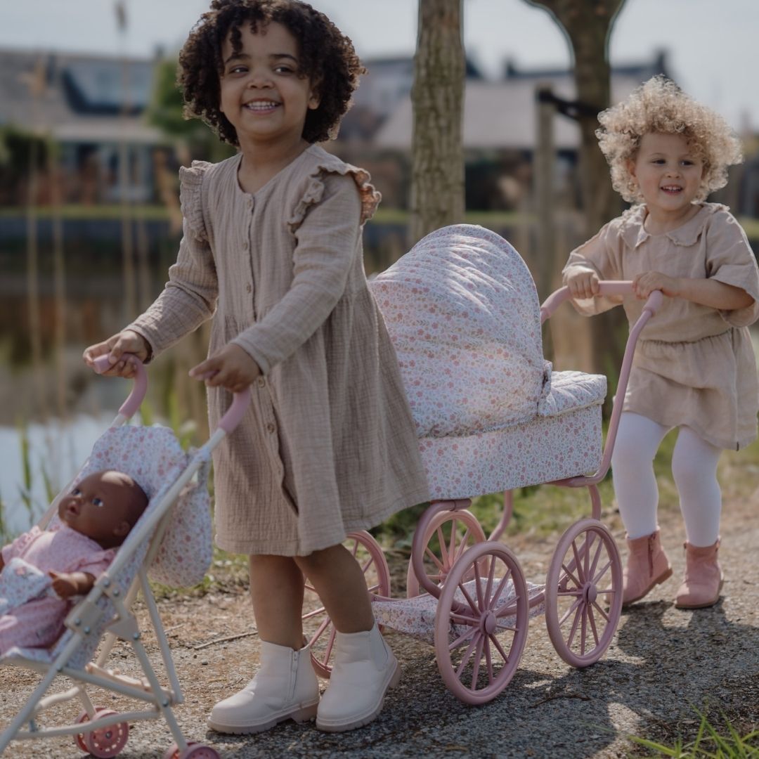 Piger leger ude med dukkevogn og barnevogn til dukke. Med rosa stel og hvidt betræk med små blomster. Flot dukkevogn til ture med dukke både ude og inde, fra Little Dutch, fås hos Nordic Simply