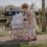 Pige ude ser til dukke i barnevogn med rosa stel og hvidt betræk med små blomster. Flot dukkevogn til ture med dukke både ude og inde, fra Little Dutch, fås hos Nordic Simply