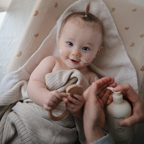 Baby med Mushie bodylotion på kinderne. Parfumefri, Svanemærket babylotion, produceret i Danmark.