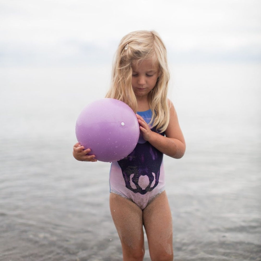 pige i badedragt med lille lilla badebold på strand