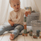 Lille dreng bygger med farverige træklodser, iført en T-shirt med dyremotiv, i en hyggelig indendørs legestue.