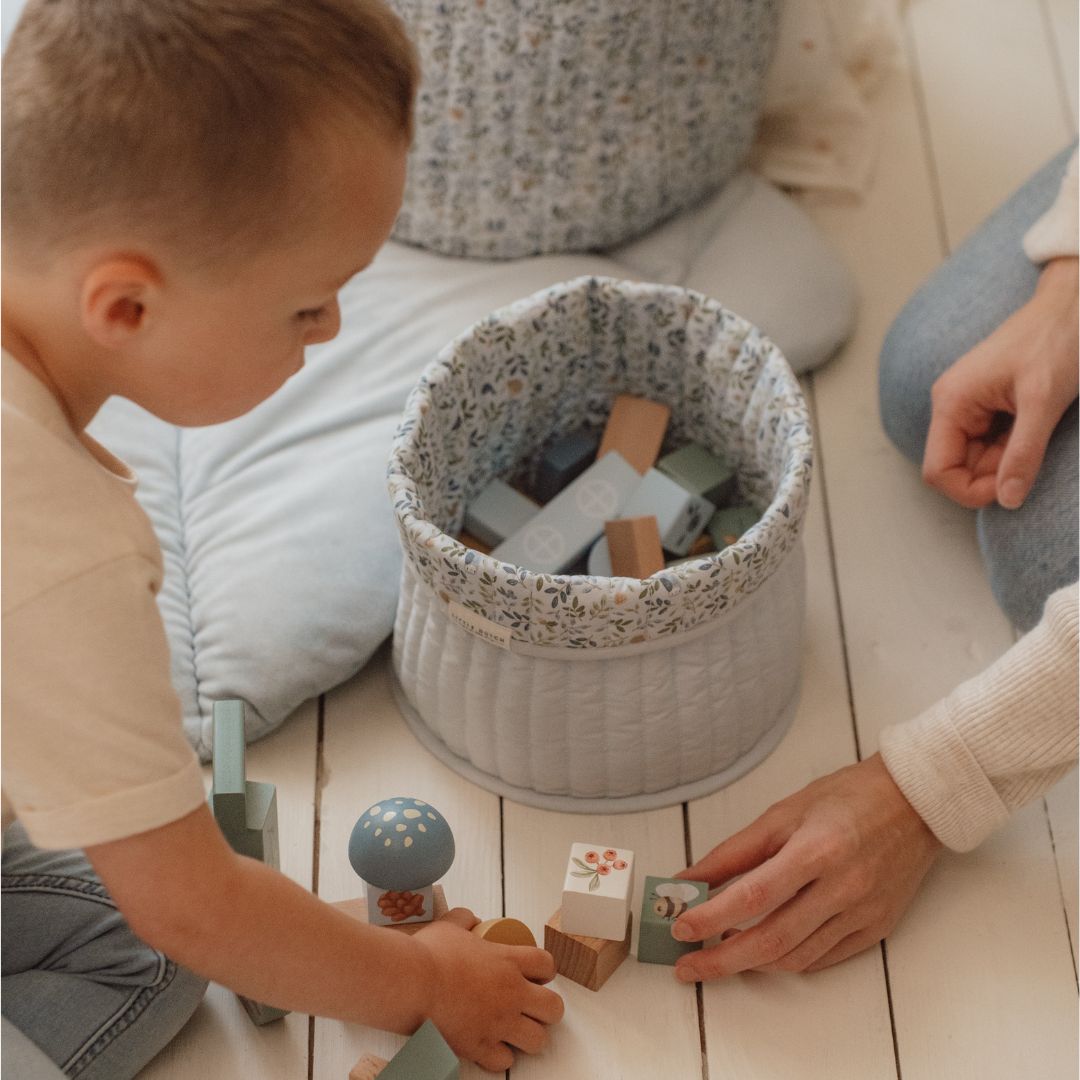 Barn leger med byggeklodser i træ fra Little Dutch i en stue med bløde puder og en opbevaringskurv.