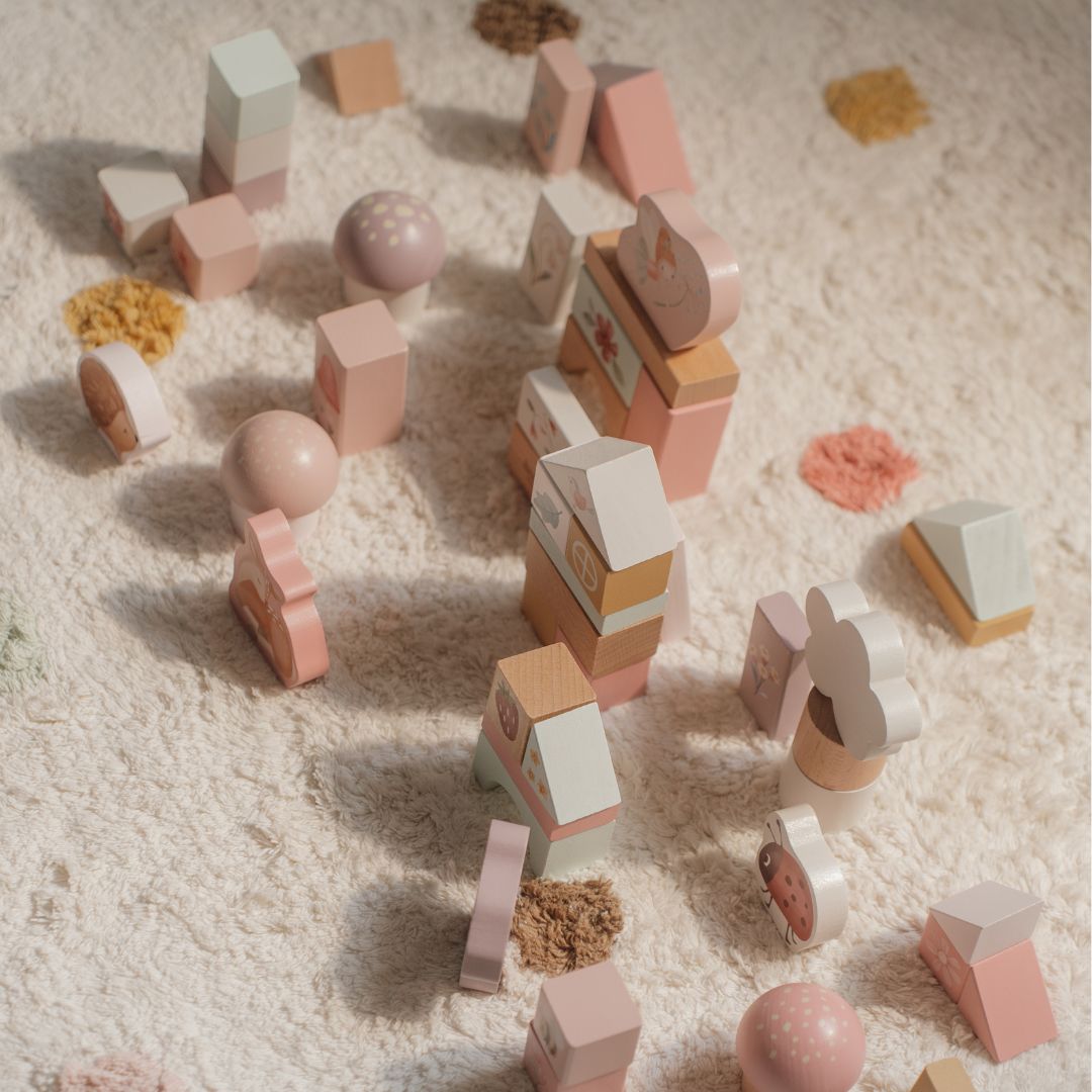 Farverige byggeklodser i rosa nuancer, træklodser med dyremotiver spredt på et blødt underlag.