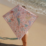 barn på strand holder rosa drage med motiver af havfruer op foran ansigtet.