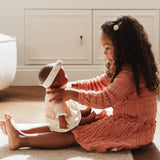 Dukke Noa med udstyr, 36 cm. En glad lille pige leger med sin livagtige dukke i et lyst, hyggeligt rum.