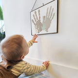 Baby kigger på 4 håndaftryk af familien, som hænger på væggen i sort ramme.
