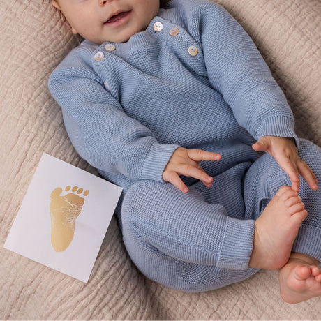 fodaftryk i guld ligger ved siden af baby i blå dragt, med bare fødder, set hos Nordic Simply