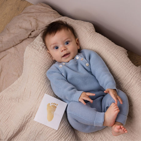 fodaftryk i guld ved baby, der ligger på lyst tæppe i blå dragt, med bare fødder, set hos Nordic Simply