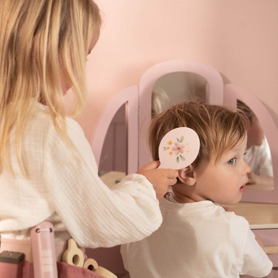 Børn leger frisør med frisørsæt i træ med hoftebælte, børste og spejl i baggrunden.