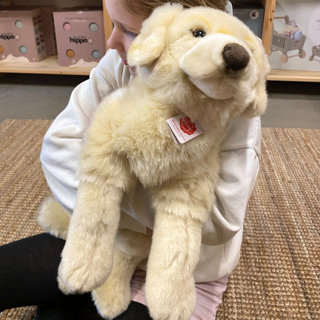 barn sidder med stor lys Golden Retriever bamse, på lyst gulvtæppe hos danske Nordic Simply - en blød og krammevenlig bamse til leg