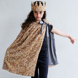 Barn i lang guldkappe og krone, skinner med tusindvis af pailletter, perfekt til udklædning.