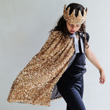 Barn i lang guldkappe med pailletter og krone, klar til leg som prins eller troldmand.