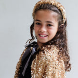 Pige smiler i lang guldkappe og krone, der skinner med tusindvis af pailletter, perfekt udklædning fra 3 til 8 år.