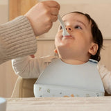 baby, med blå hagesmæk med opsamlingslomme og sødt motiv af ræv, får mad med ske.