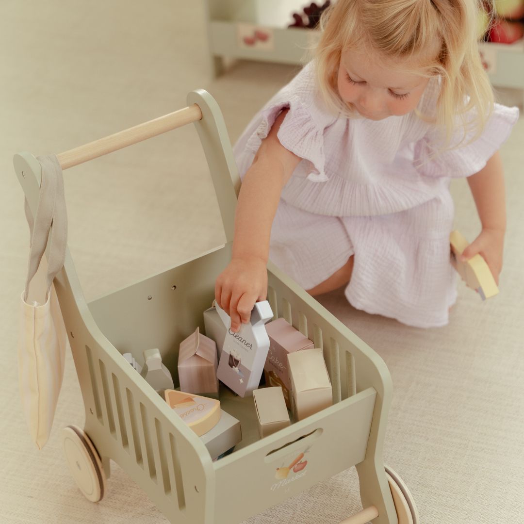 Lille pige fylder sin indkøbsvogn i træ fra Little Dutch med varer til sjov rolleleg. Perfekt til eventyr og butiksleg.