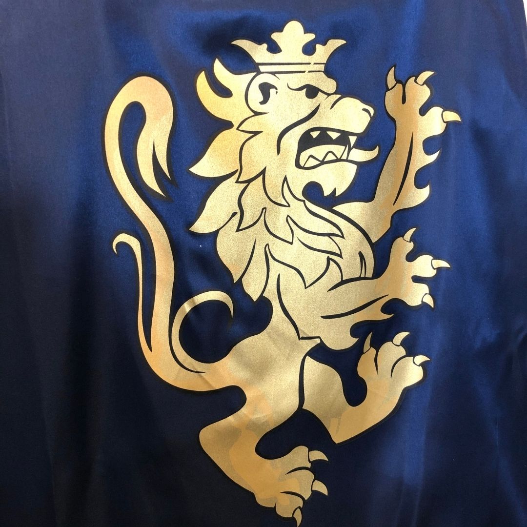 Blå kappe til ridder set tæt på med løve i guld. Flot skinnende blå ridderkappe Noble Knight, fra LionTouch, fås hos Nordic Simply