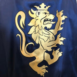 Blå kappe til ridder set tæt på med løve i guld. Flot skinnende blå ridderkappe Noble Knight, fra LionTouch, fås hos Nordic Simply