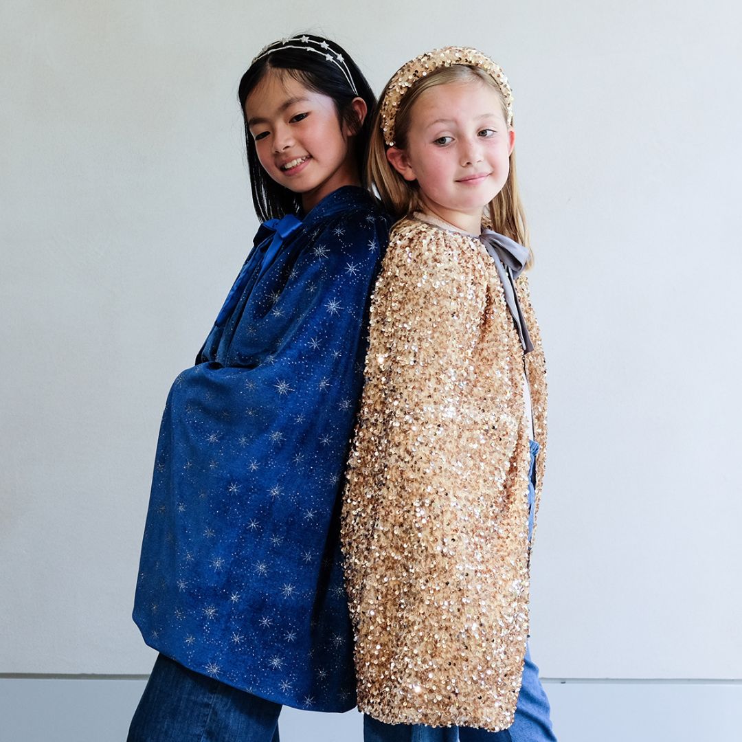 To børn iført lang blå velour kappe med stjerner og lang guldkappe, fra Mimi & Lula, står ryg mod ryg.