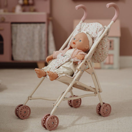 Klapvogn rosa til ture med dukke med en dukke iført blomsteroutfit i en stue.