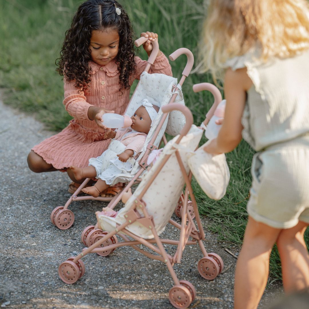 to piger hygger om deres dukker, der sidder i smukke dukke klapvogne med rosa håndtag og fint blomstermotiv