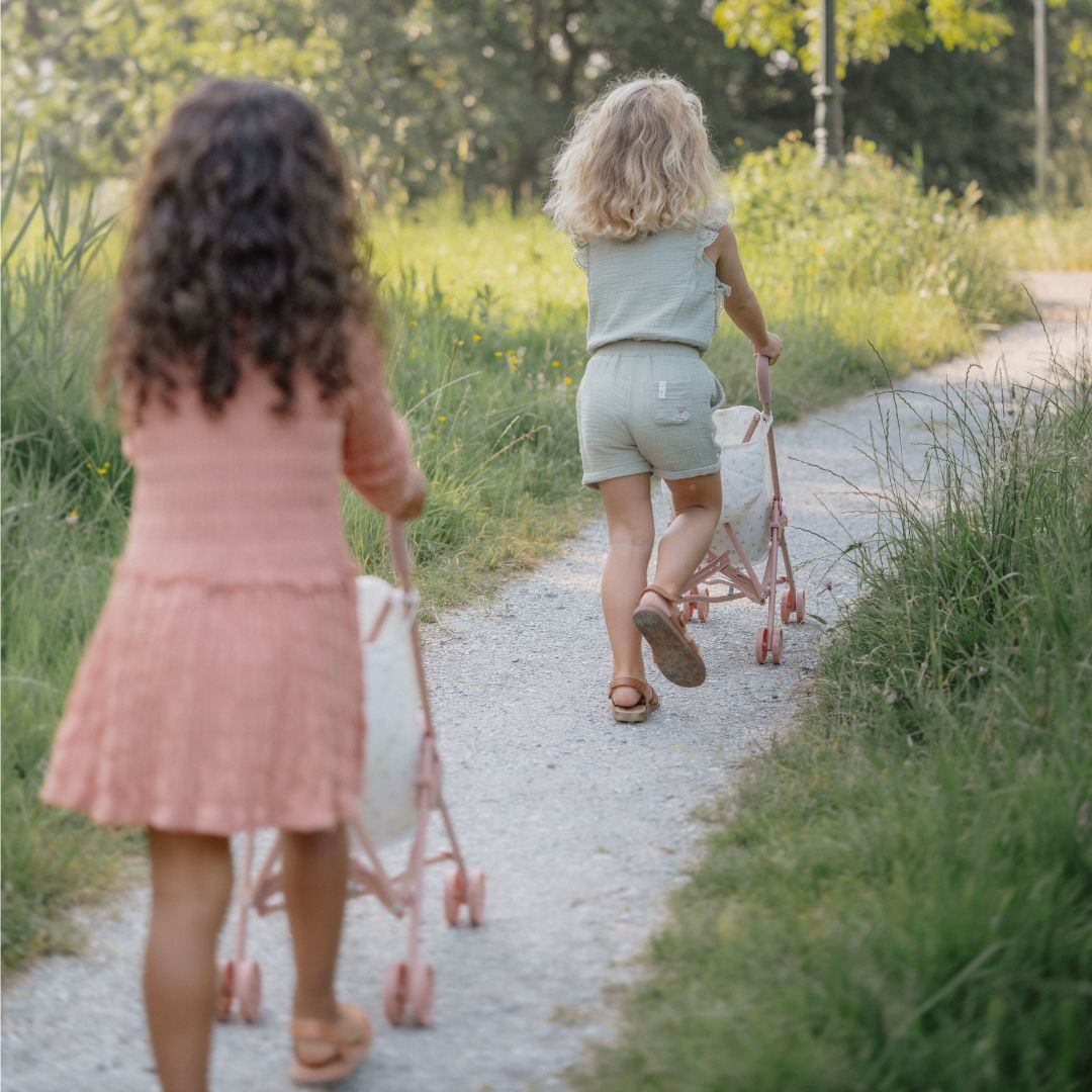 to piger set bagfra, går tur på sti med dukker i smukke dukke klapvogne med rosa håndtag og fint blomstermotiv
