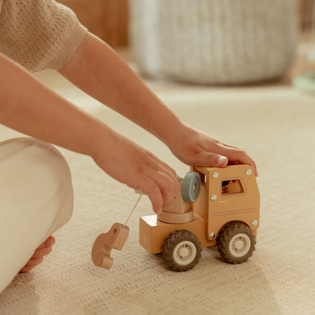 Kranbil med træfigur i brug, her set med barn, der leger med den robuste kranbil med gummihjul på lyst gulvtæppe