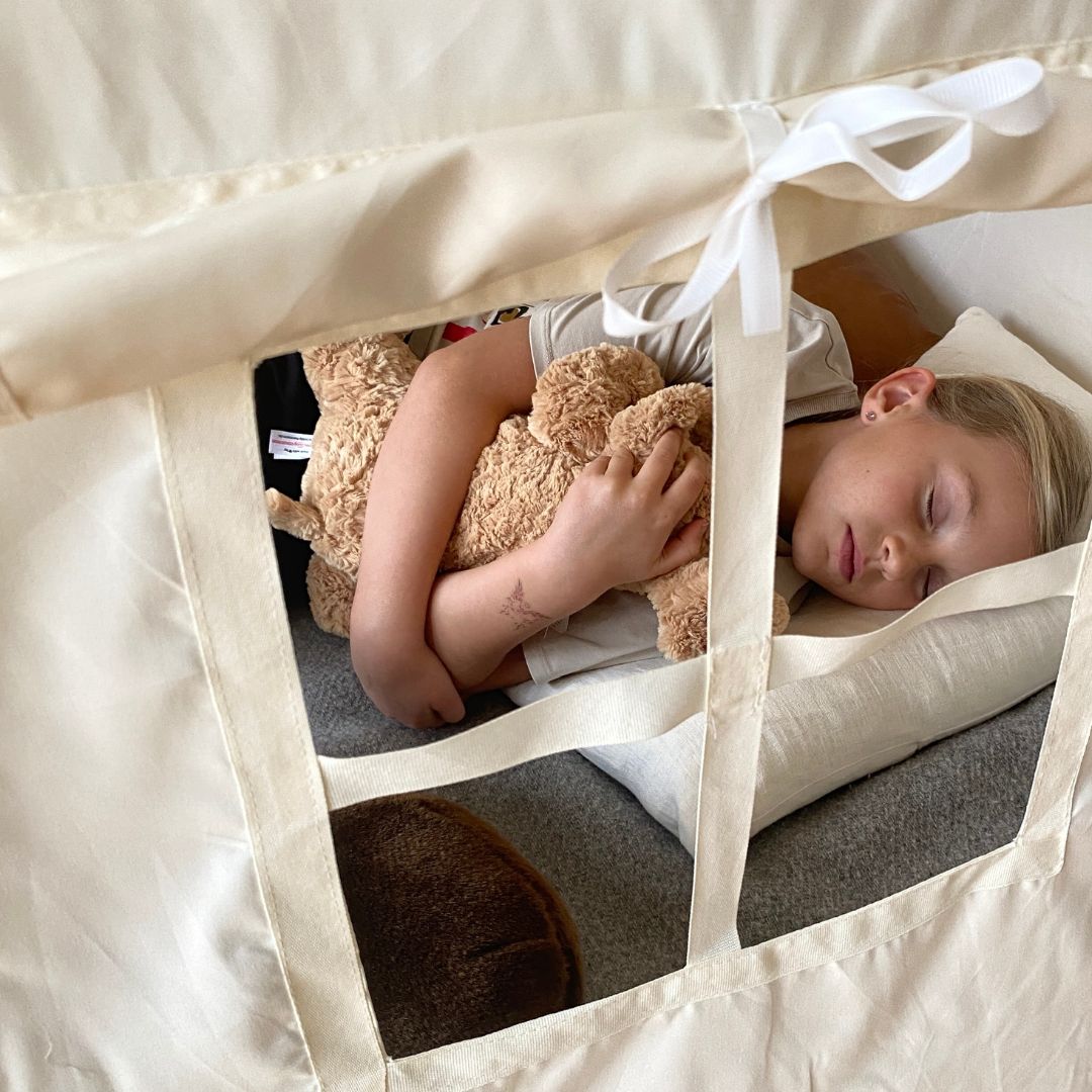Pige sover i beige legetelt sammen med bamsehunde - set udefra ind ad vindue. Et flot legetelt til pige og dreng til fantasifuld leg og hyggelige stunder.