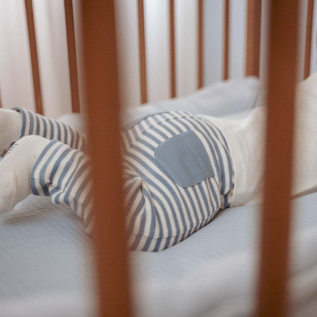 baby set bagfra ligger i babyseng med blå og hvid stribede baby leggings med blå lommer. Søde babybukser til lille dreng eller pige.