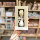 Hånd holder gaveæske med beige og hvid maracas i træ fra BamBam med rundt BamBam logo. Dejligt lille instrument til barn fra 18 måneder, fås hos Nordic Simply.