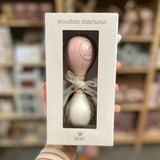 Hånd holder gaveæske med rosa og hvid maracas i træ fra BamBam med rundt BamBam logo. Dejligt lille instrument til tumling og barn fra 18 måneder og op, fås hos Nordic Simply.