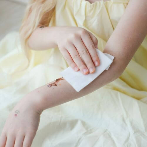 A child gently wipes away a temporary tattoo on their arm, showcasing playful creativity and fun in self-expression.