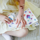 Little girl applying colorful stickers and temporary tattoos while sitting on the floor, showcasing creativity and fun.