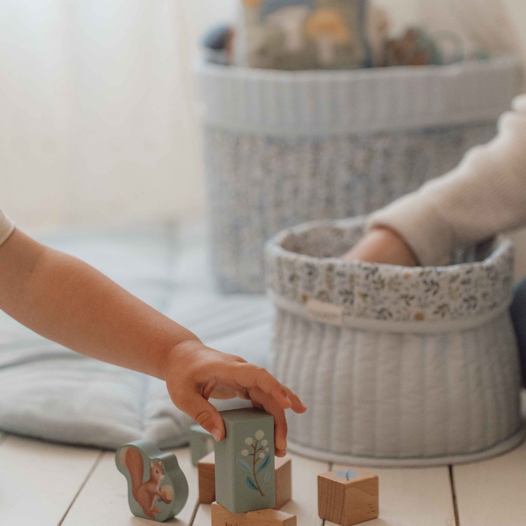 2 runde opbevaringskurve i lyseblå med blomstret ombukket kant, 1 stor kurv og 1 lille kurv står på gulv, hvor barn leger med klodser. Kurvene er quiltet  i 100% økologisk bomuld og kan vendes. Fra Little Dutch Forest Adventure kollektion.