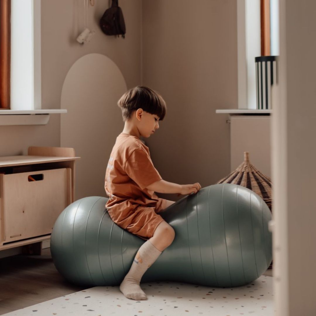 Barn sidder på blå peanutformet balancebold til sanseleg, motorisk udvikling og balance.