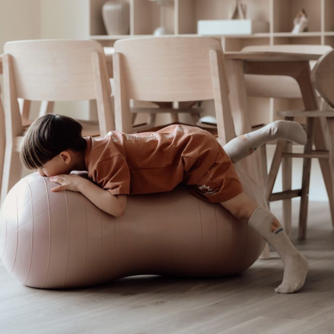 Peanut balancebold i rosa: Barn leger aktivt på en peanut-formet balancebold indendørs, fås hos Nordic Simply.