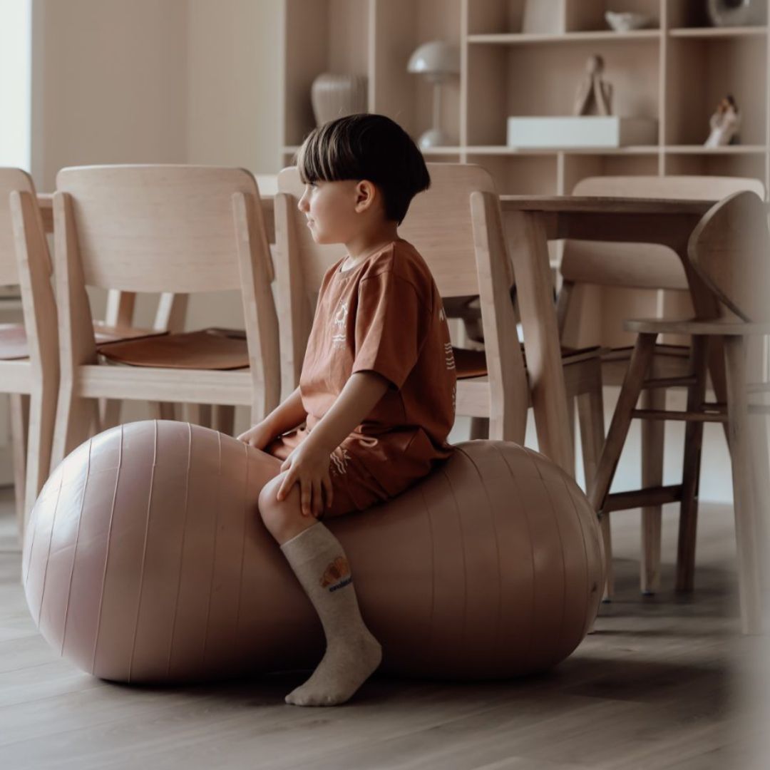 Barn sidder på peanutformet balancebold i lys rosa til sanseleg, motorisk udvikling og balance.
