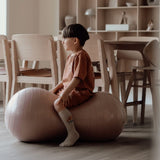 Barn sidder på peanutformet balancebold i lys rosa til sanseleg, motorisk udvikling og balance.
