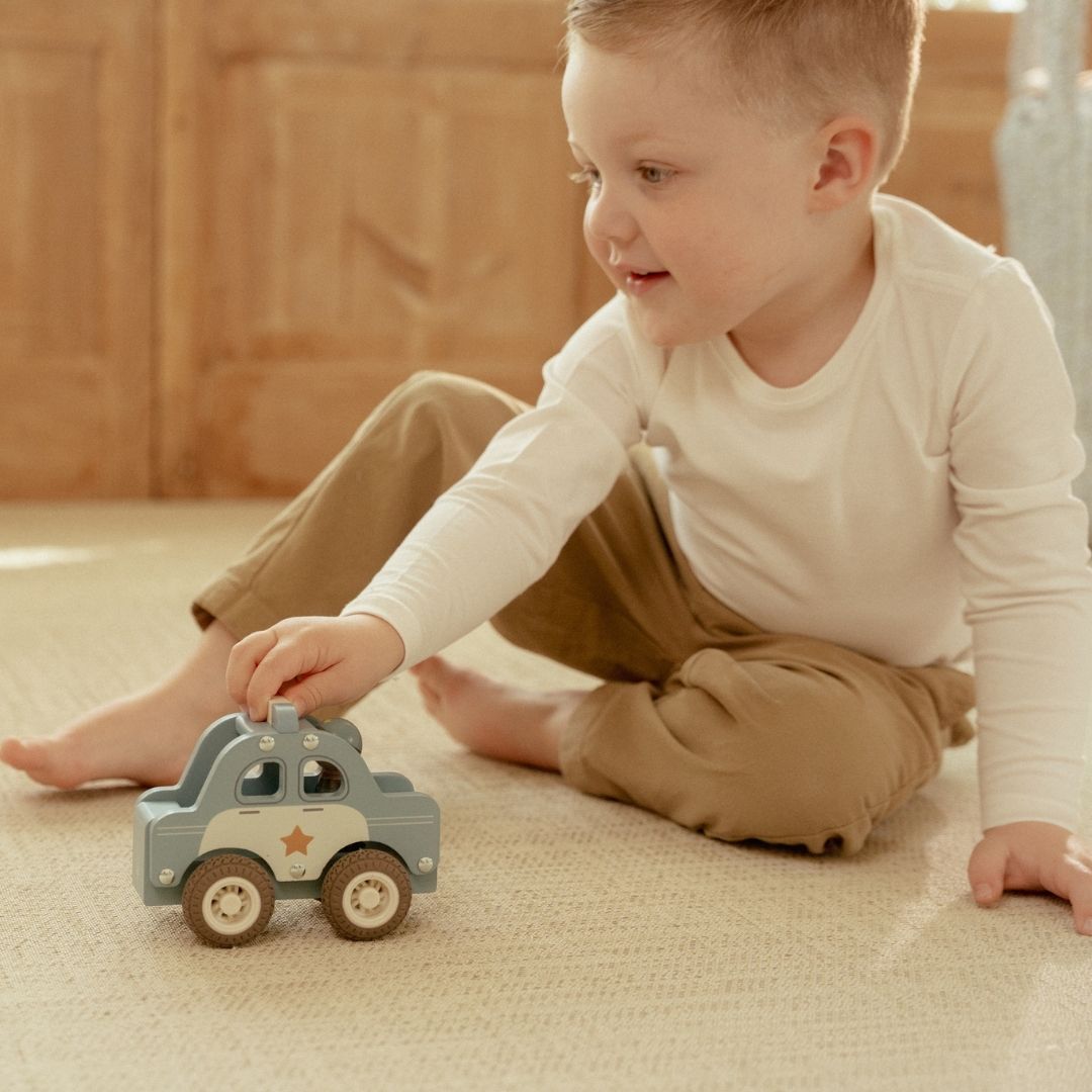 Barn der leger med en politibil med træfigur på gulvet, klar til at fange røvere