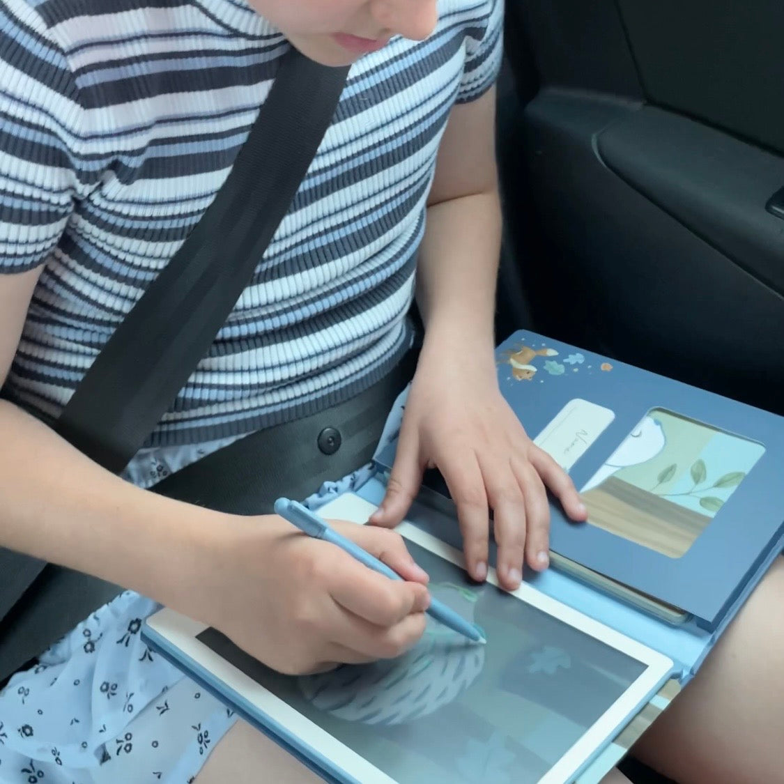 To piger tegner på hver sin tegnetablet i bil på vej på ferie, den ene pige på en blå tegnetablet, den anden pige på en rosa tegnetablet, fås hos Nordic Simply