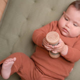 Regnmager grøn sanselegetøj. baby leger med trælegetøj på en sofa i en brun dragt.