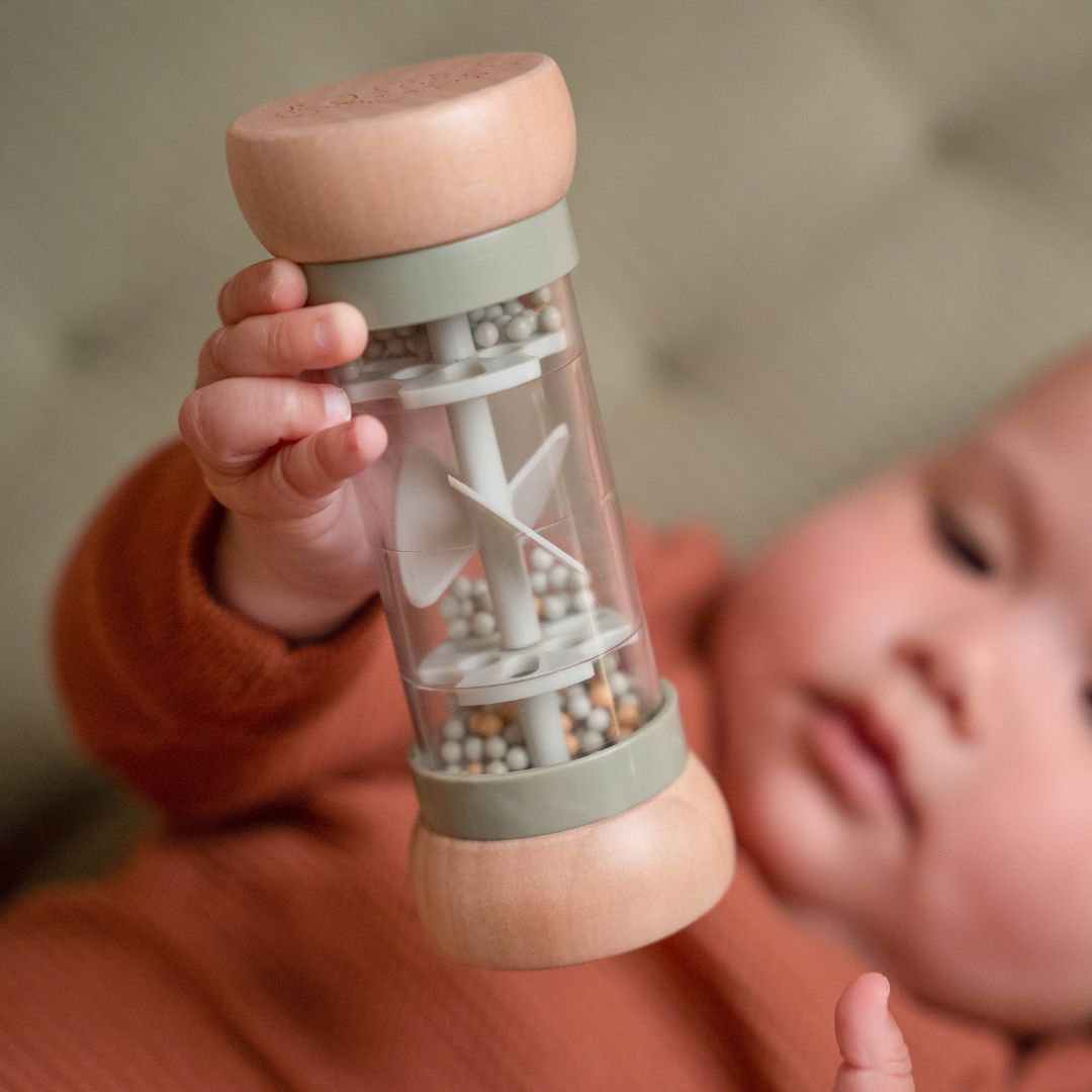 Barn der holder regnmager grøn sanselegetøj i træ med perler der rasler, stimulerer babys sanser.
