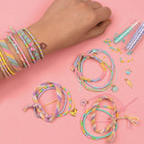 Hånd med farverige armbånd og DIY smykkesæt til at skabe 20 regnbue armbånd, inklusive charms og perler.