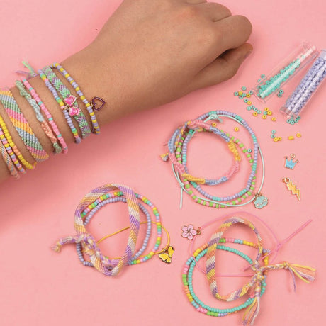 Hånd med farverige armbånd og DIY smykkesæt til at skabe 20 regnbue armbånd, inklusive charms og perler.