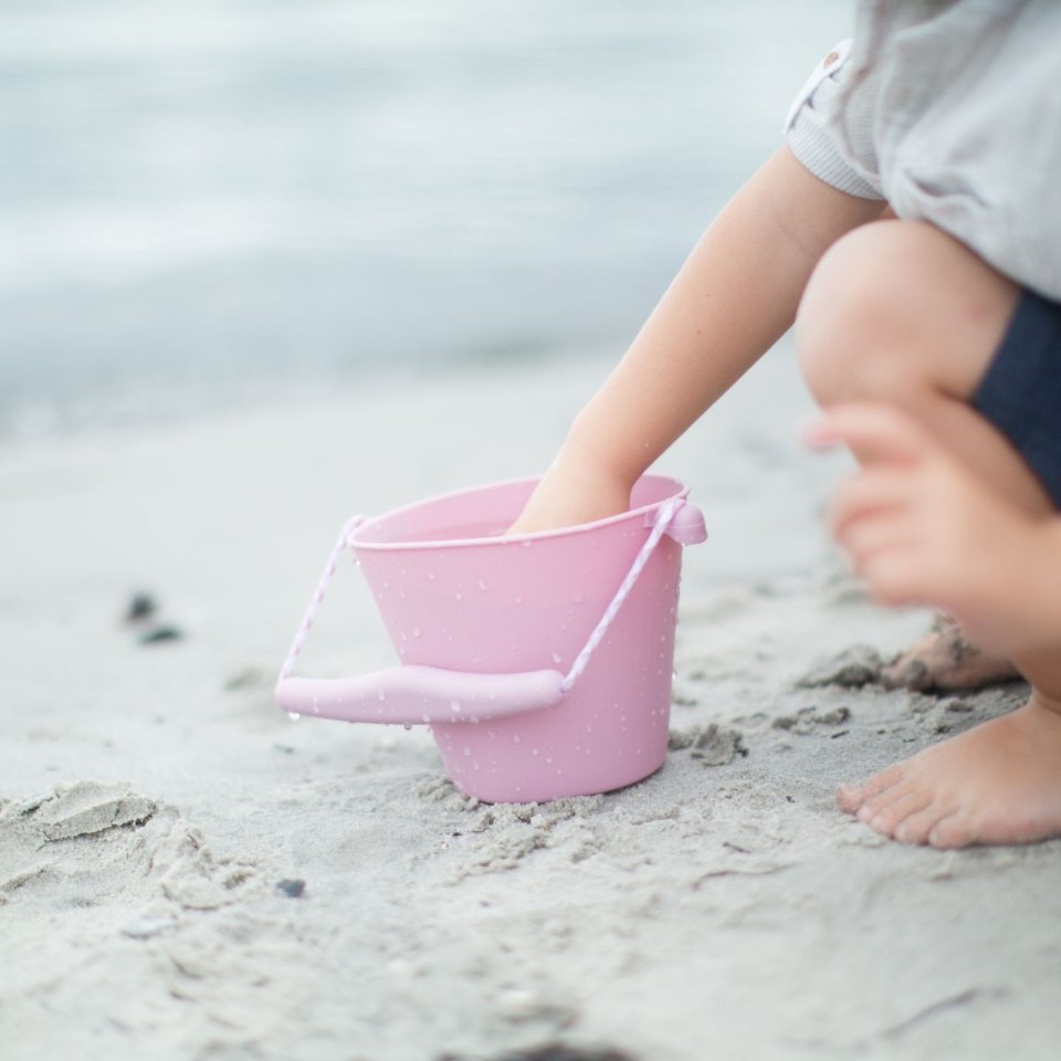 Barn leger på strand med rosa spand i silikone, kan foldes, god til ferie og rejser