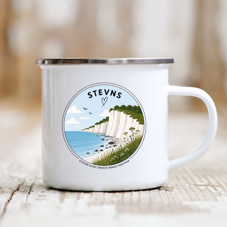 Stevns-koppen står på bord. Koppen er hvid med håndtag og har smuk illustration af Stevns Klint på forsiden
