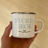 Hånd holder Storebror kop i hvid metal med blå bogstaver. God søskendegave til nybagt storebror.