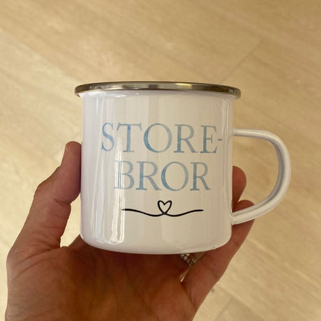 Hånd holder Storebror kop i hvid metal med blå bogstaver. God søskendegave til nybagt storebror.