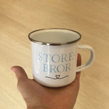 Hånd holder Storebror kop i hvid metal med blå bogstaver og hjerte. God søskendegave til nybagt storebror.